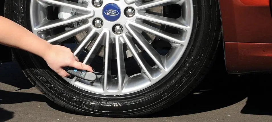 Checking tire pressure on a Ford wheel with a gauge, ensuring proper car maintenance.