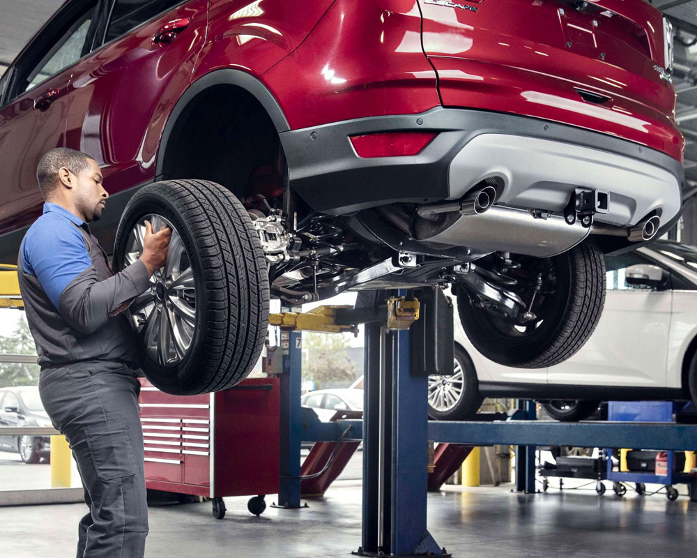 Mechanic replacing tire on red SUV raised on lift in auto repair shop.