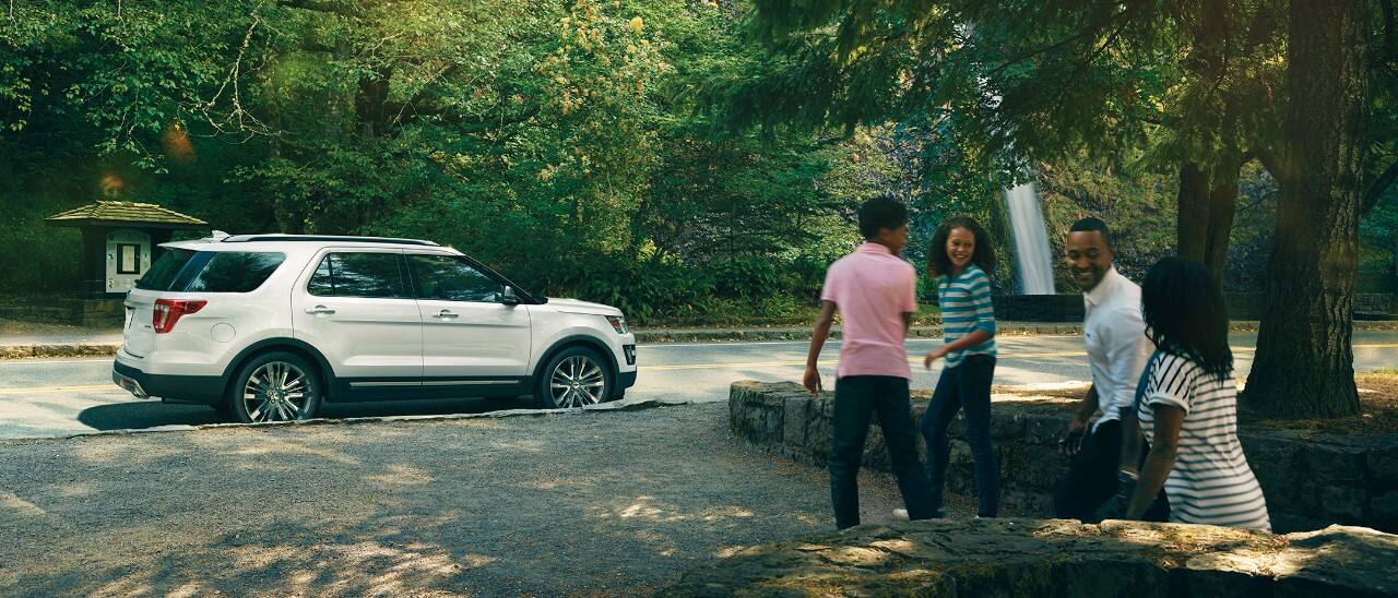 Family enjoys time near a parked white SUV in a scenic forest setting, emphasizing outdoor adventure.