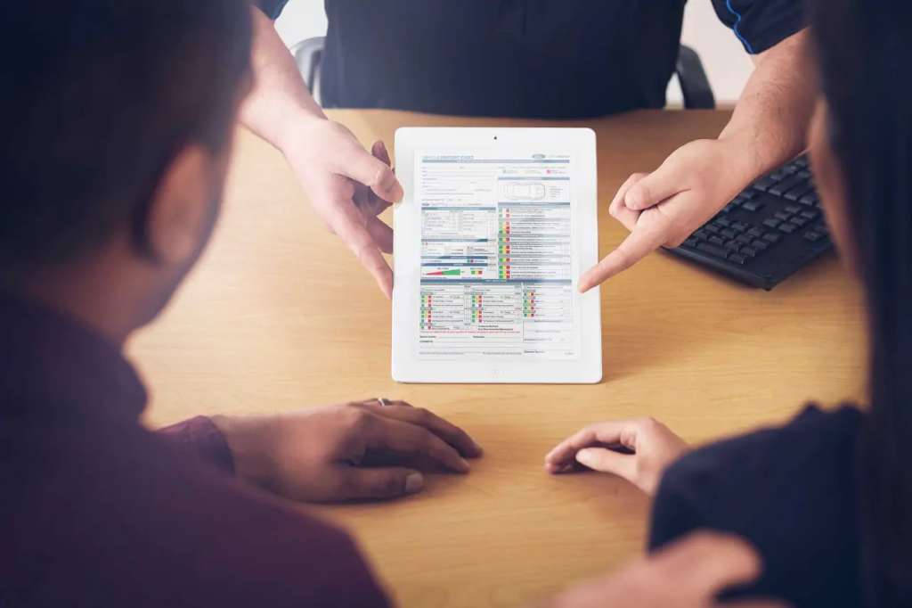 People reviewing a vehicle report on a tablet at a wooden desk, emphasizing analysis.