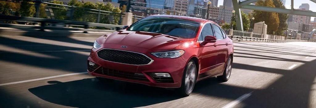 Red Ford sedan driving on a city bridge, showcasing sleek design and urban efficiency.
