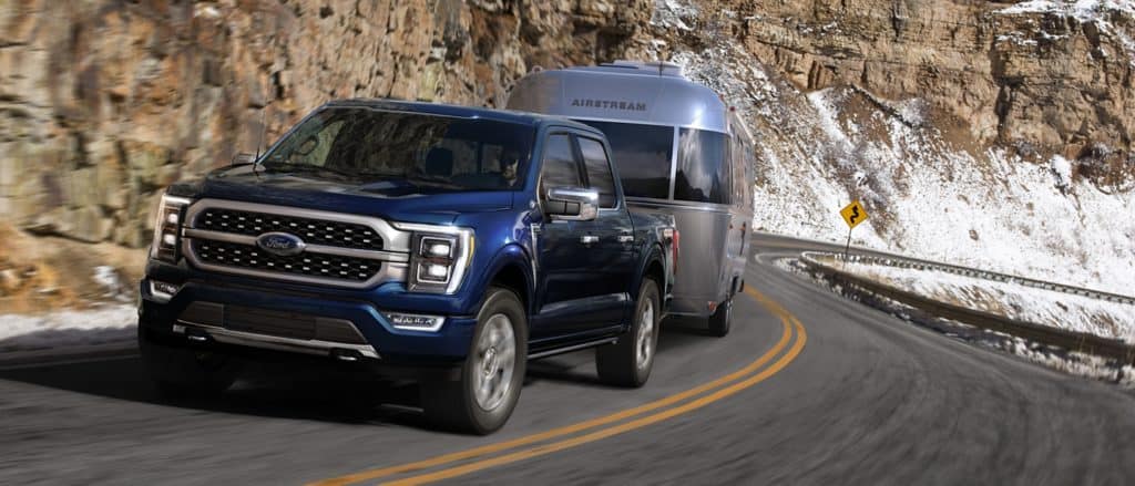 Blue Ford truck towing an Airstream trailer on a snowy mountain road.